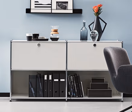 Pokój z antracytowym krzesłem biurowym i metalowymi szafkami typu sideboard. Jedna antracytowa i dwie białe metalowe szafki typu sideboard CN3 z 2 klapami do indywidualnego rozmieszczenia.