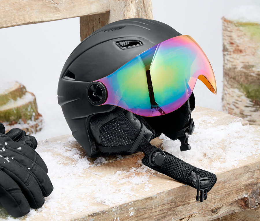 Kask narciarski i snowboardowy typu hardshell z wizjerem leży na drewnianej ławce. Obok leżą czarne rękawice.