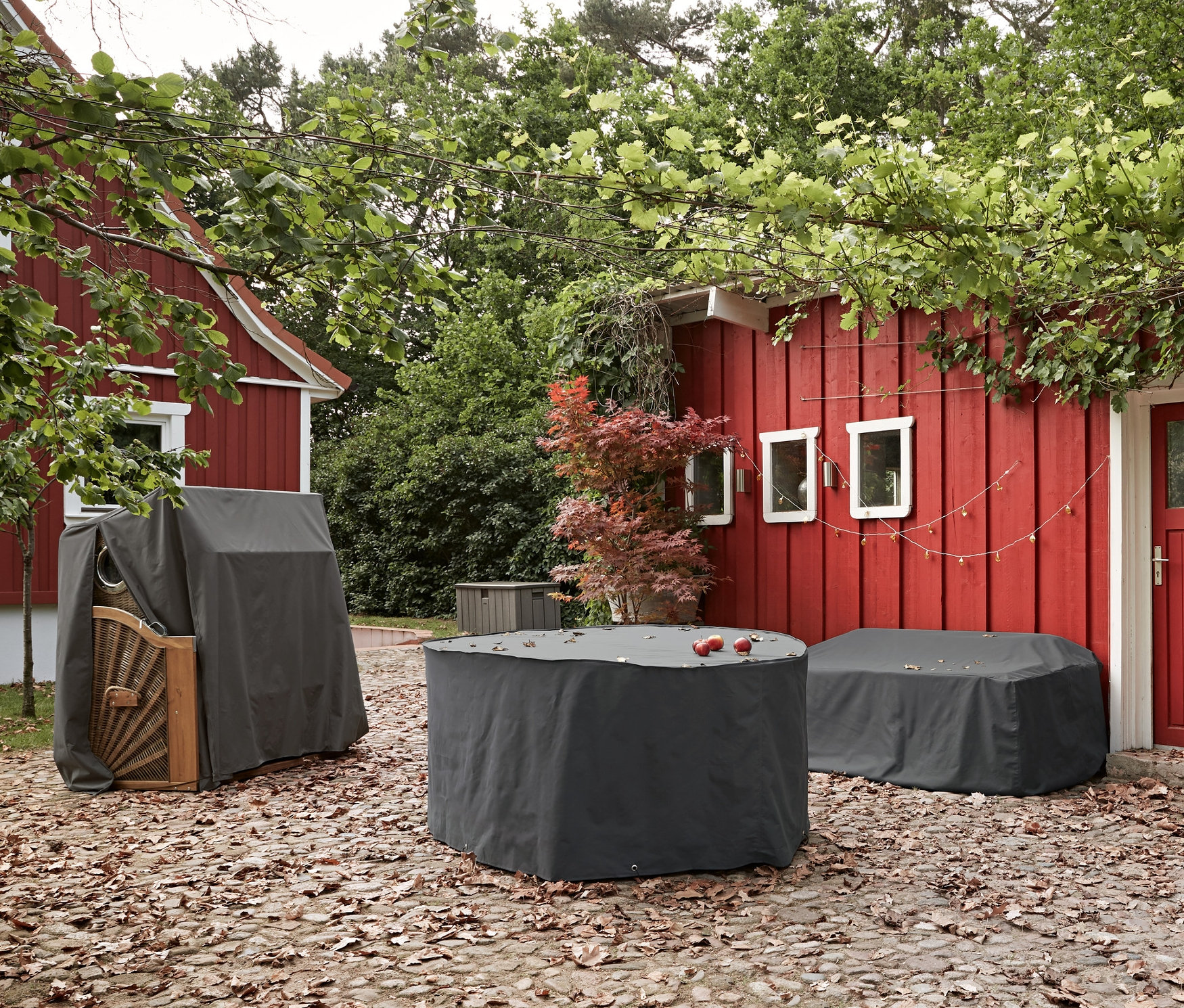 Na wybrukowanym tarasie znajdują się pokrowce na meble ogrodowe, wodoszczelny pokrowiec na sofę ogrodową i pokrowiec na kosze plażowe.