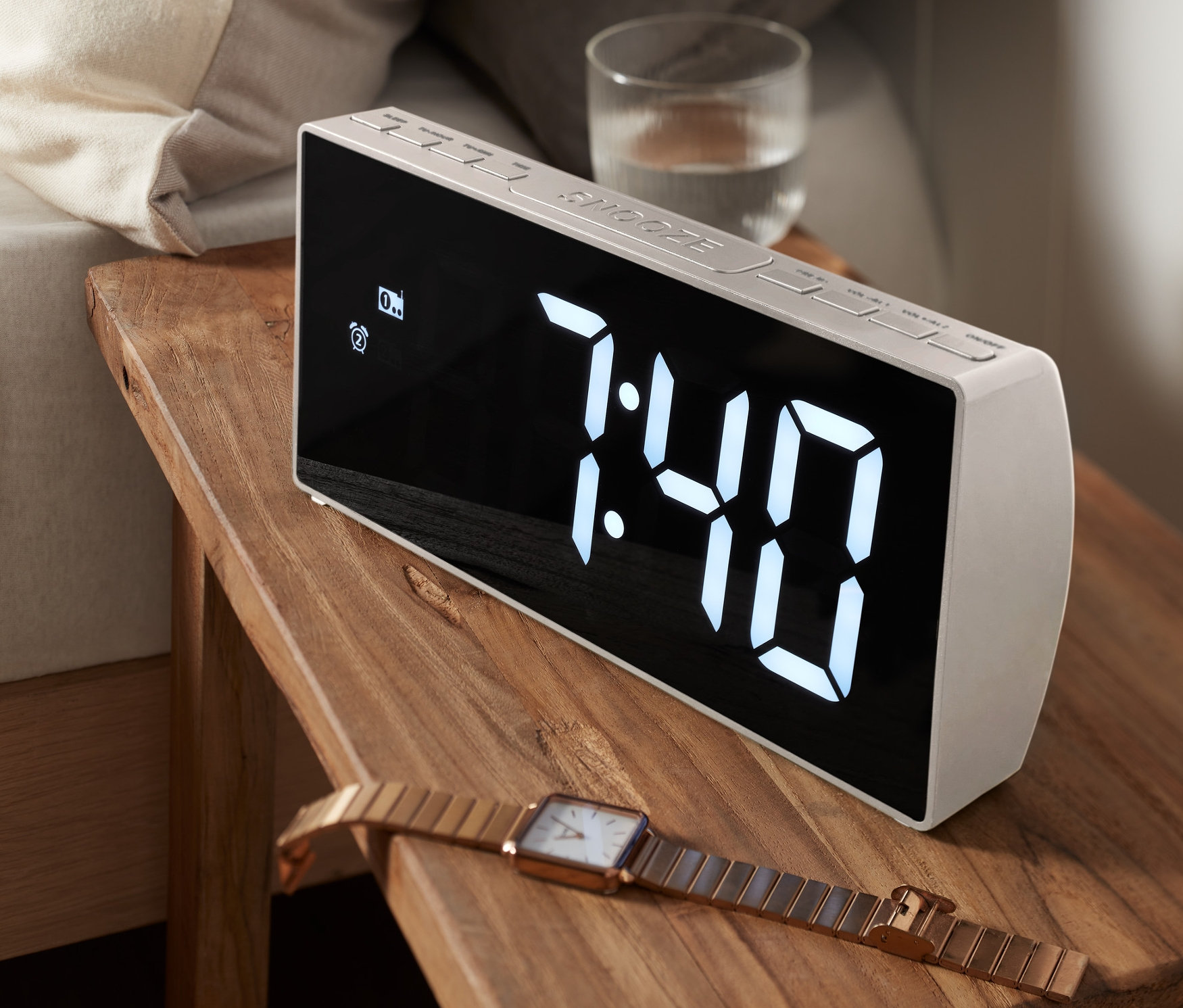 Radiobudzik XXL stoi na drewnianym stoliku nocnym obok łóżka. Na wyświetlaczu widnieje godzina 7:40.