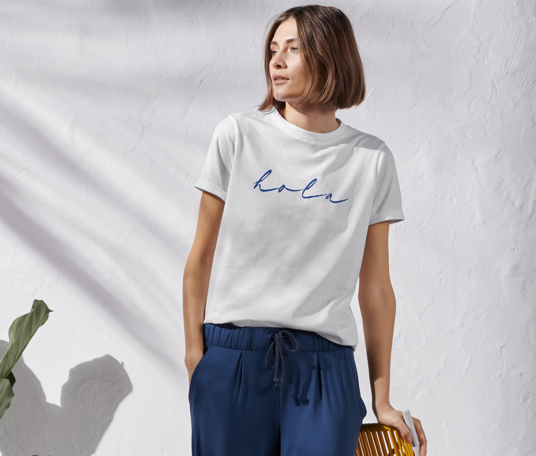 Kobieta stoi w białej koszulce z nadrukiem i niebieskich spodniach.