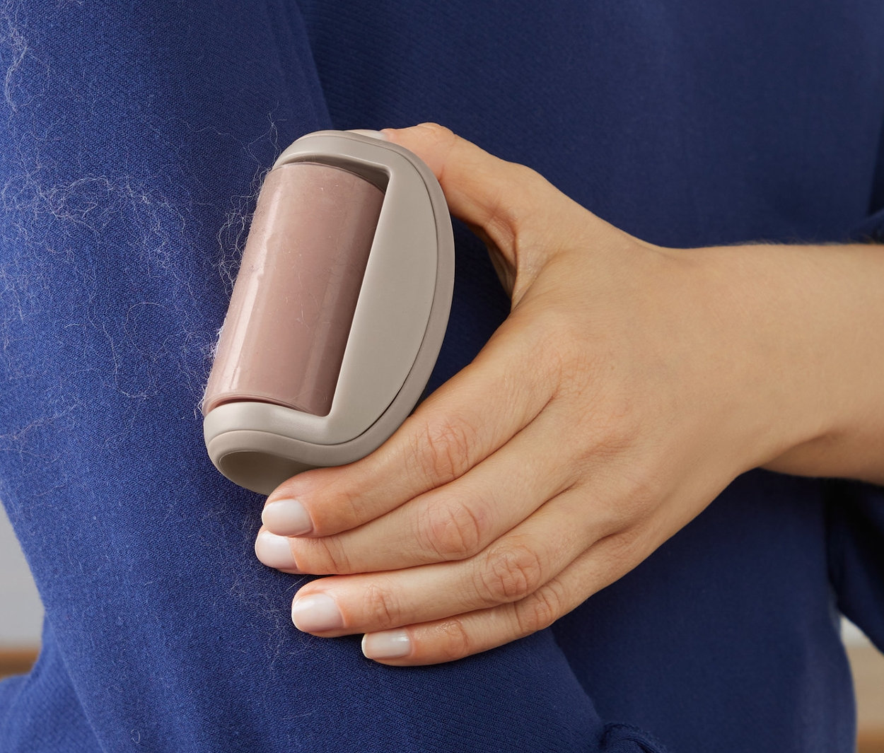 Kobieta używa rolki do czyszczenia odzieży na niebieskim swetrze.