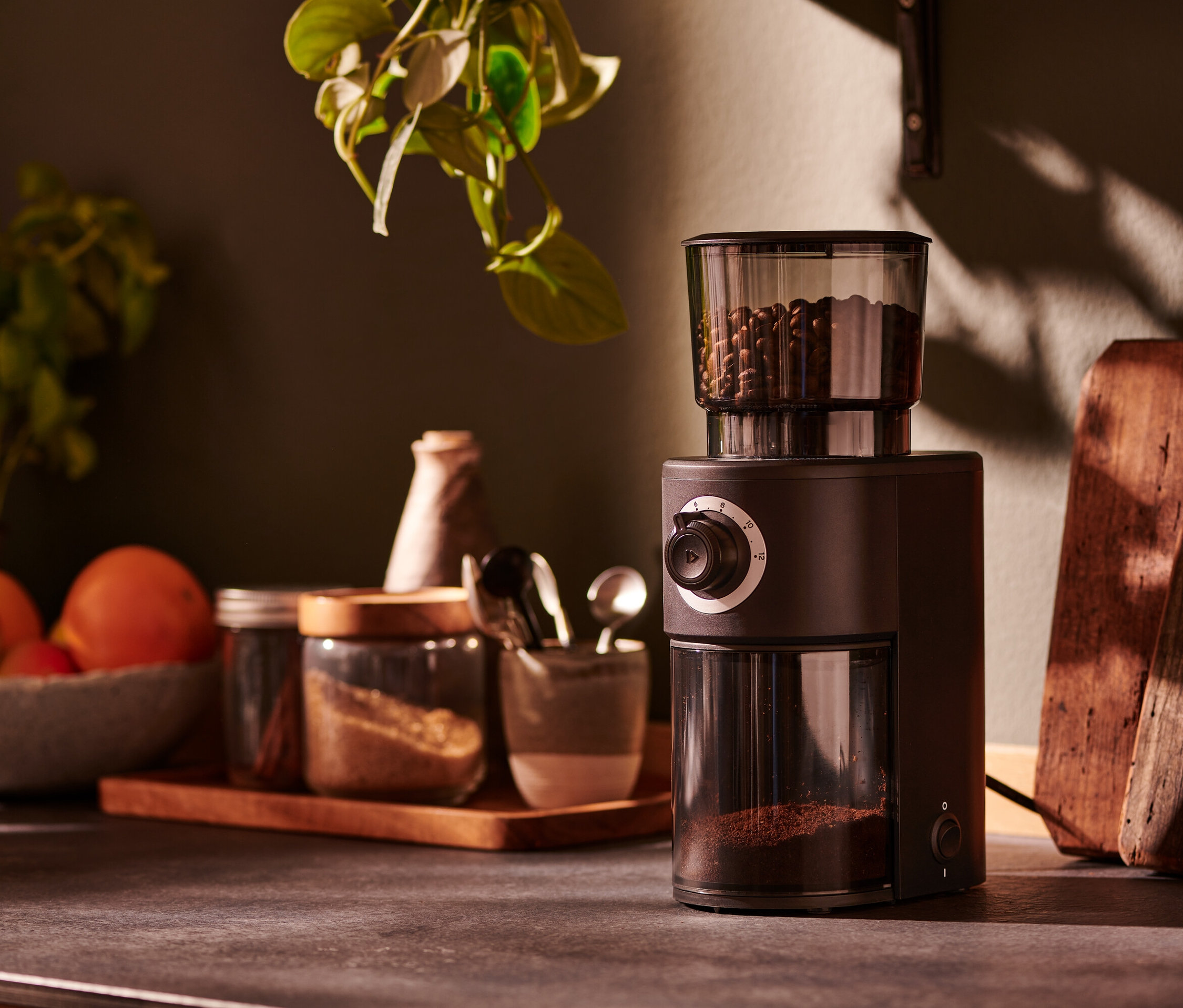 Brązowy elektryczny młynek do kawy stoi na blacie kuchennym obok słoików z przyprawami.
