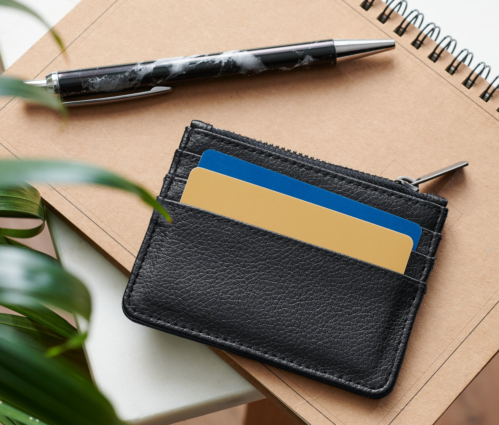 Czarne etui na karty leży na notatniku obok długopisu.