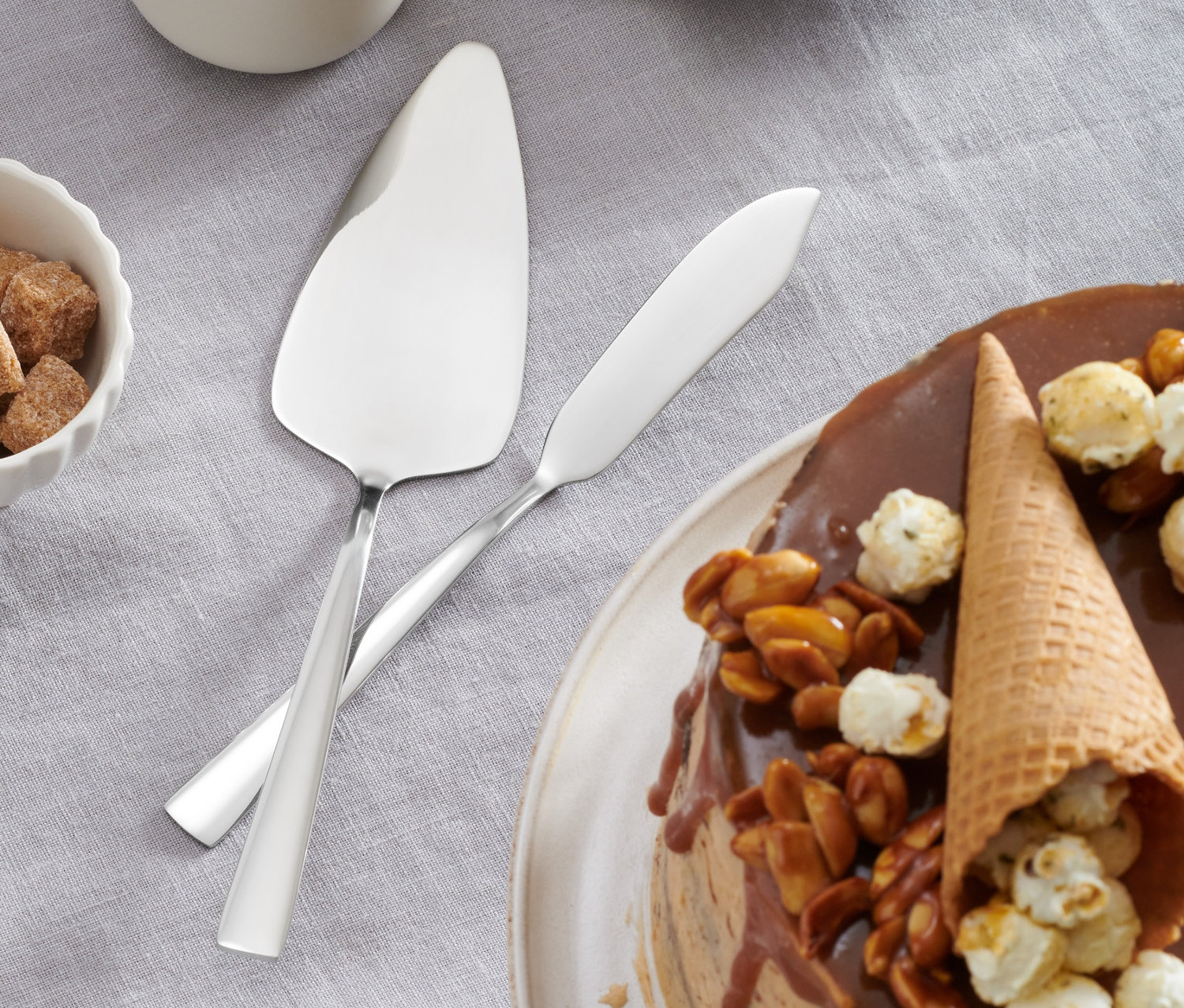 Na stole leży tort z polewą, orzechami i popcornem obok 2-częściowego zestawu sztućców do tortu.