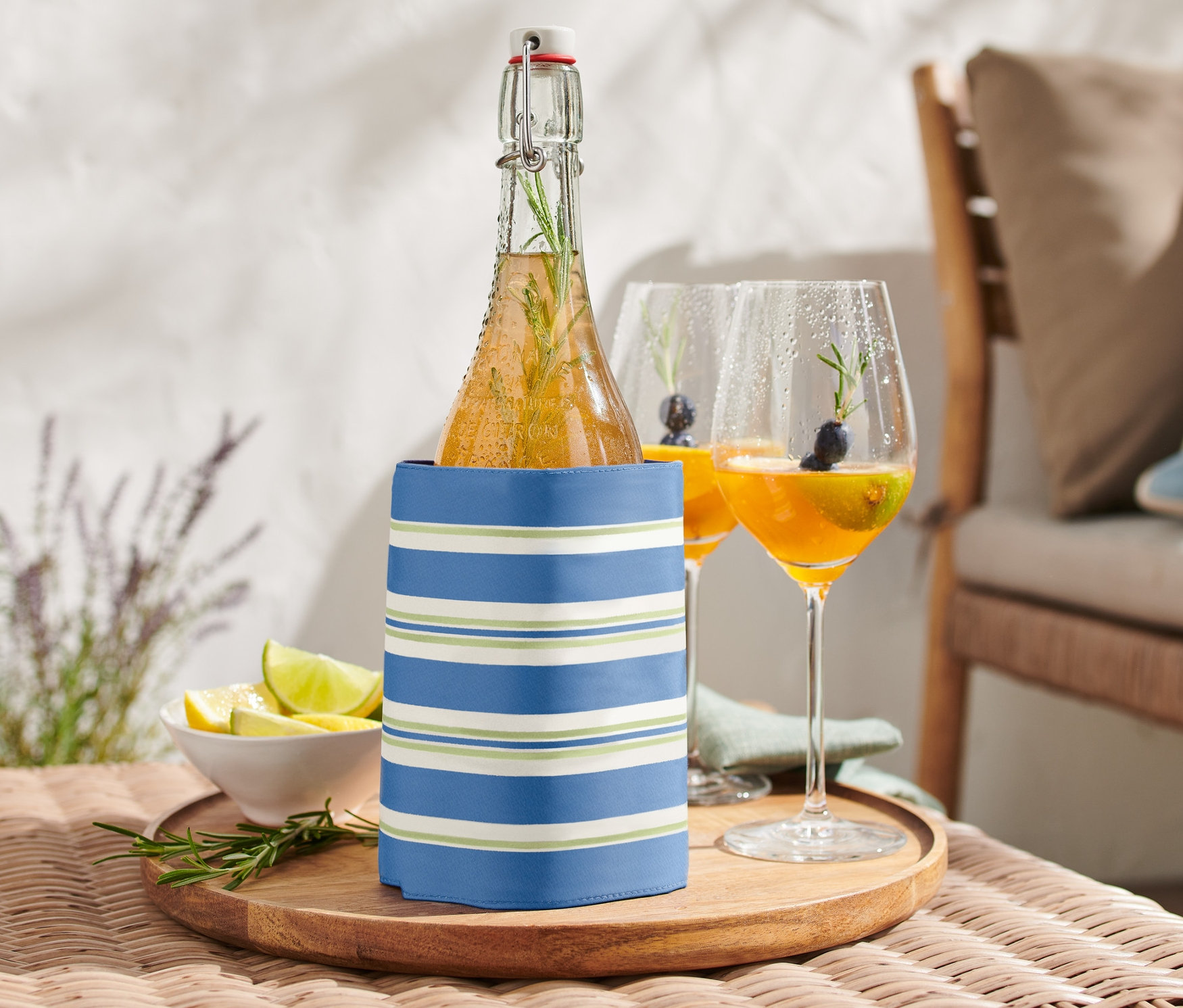 Butelka w kołnierzu chłodzącym na stole obok dwóch szklanek z napojem.