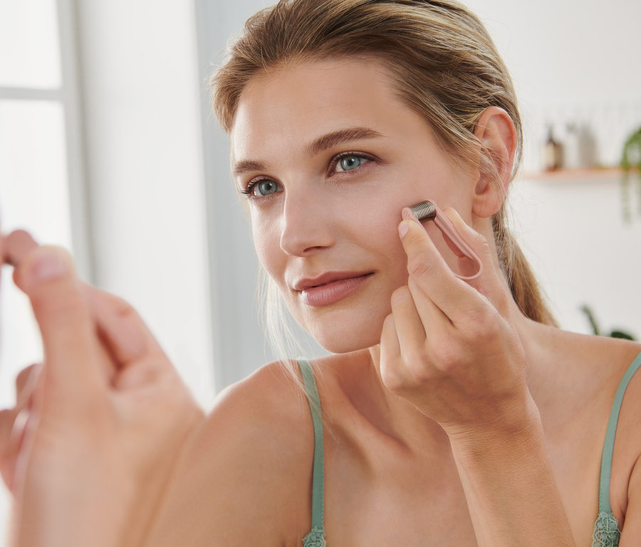 Kobieta używa mini depilatora do twarzy przed lustrem.