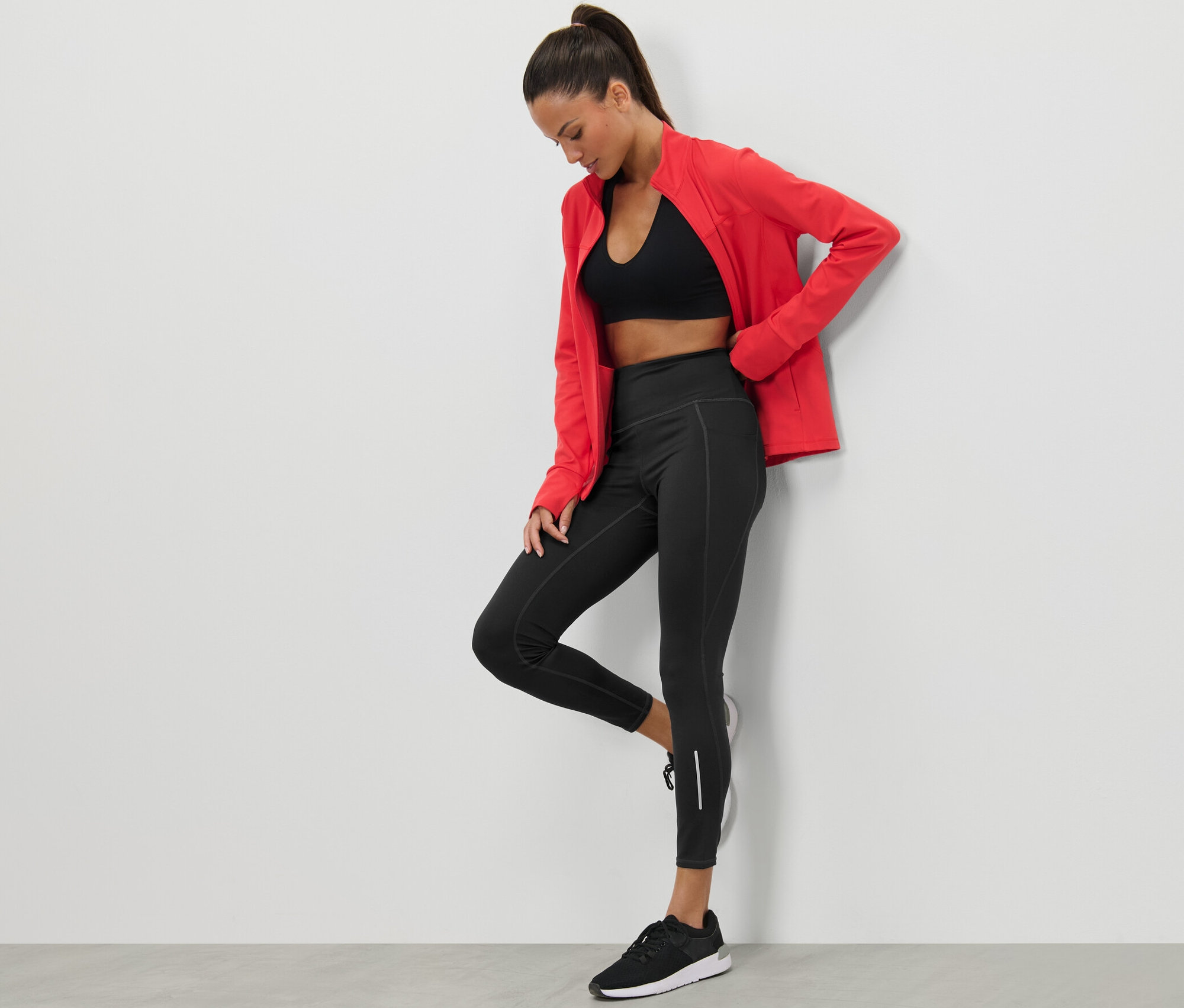 Kobieta pozuje w czarnych legginsach sportowych i czerwonej kurtce.