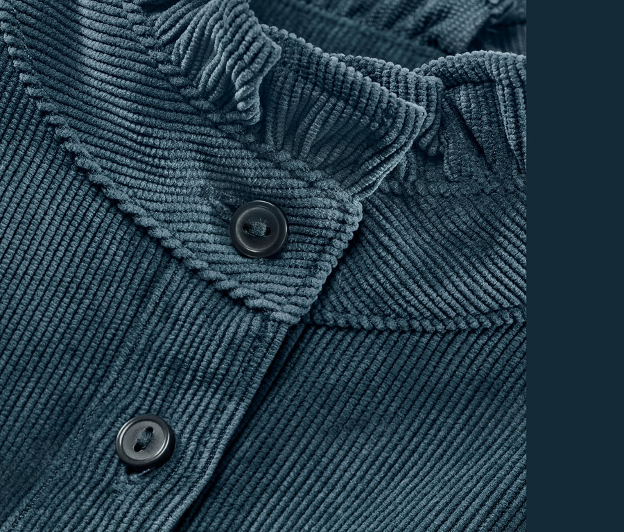 Zbliżenie na niebieską bluzkę sztruksową z falbanką i guzikami.