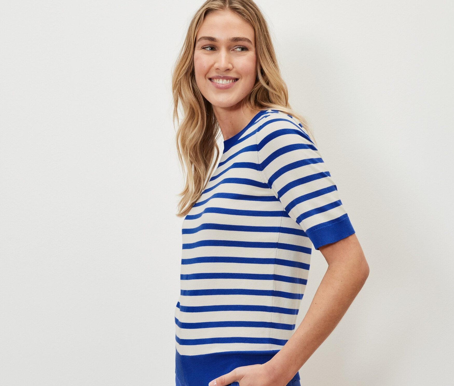 Kobieta ma na sobie cienki sweter w paski i niebieskie spodnie.