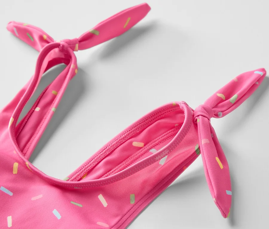 Zbliżenie na różowe bikini w kolorowe posypki dla dzieci, wiązane na ramiączkach.