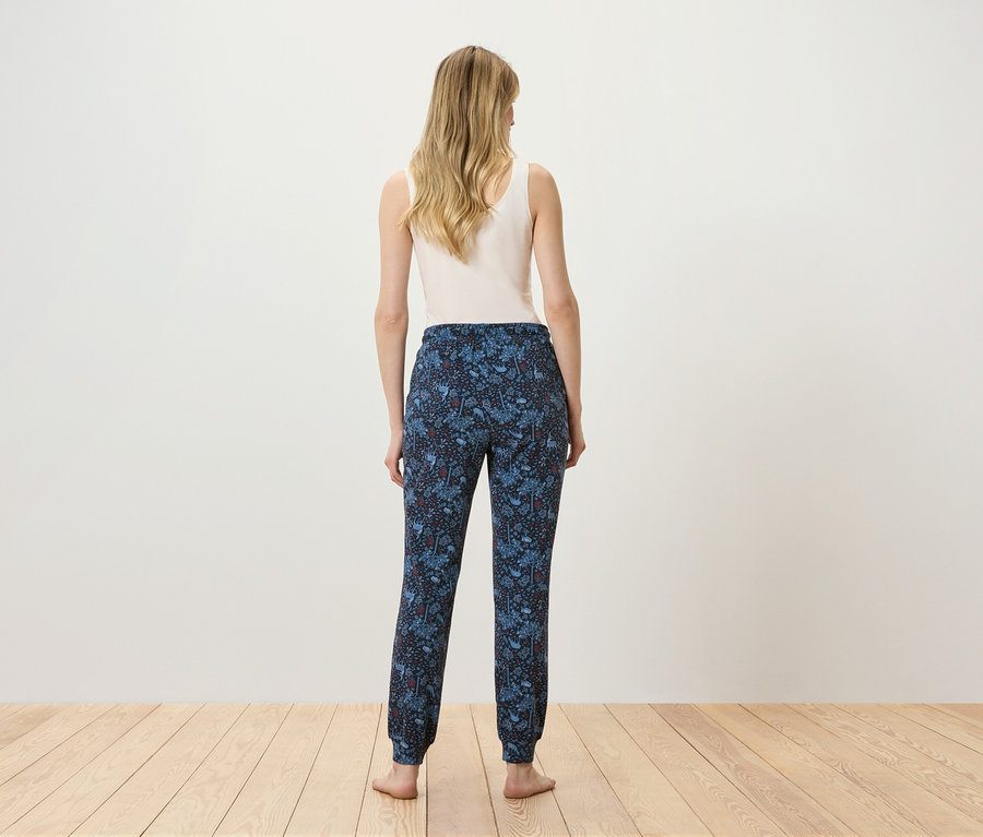 Kobieta stoi tyłem do kamery, ubrana w biały top i niebieskie spodnie we wzory.