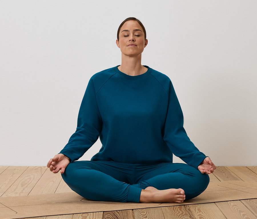 Kobieta siedzi w siadzie skrzyżnym na macie do jogi i medytuje.