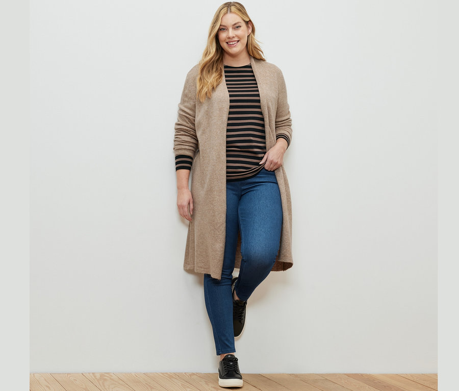 Kobieta pozuje w jegginsach, pasiasta koszulka z długim rękawem, czarno-brązowa i długim kardiganie.