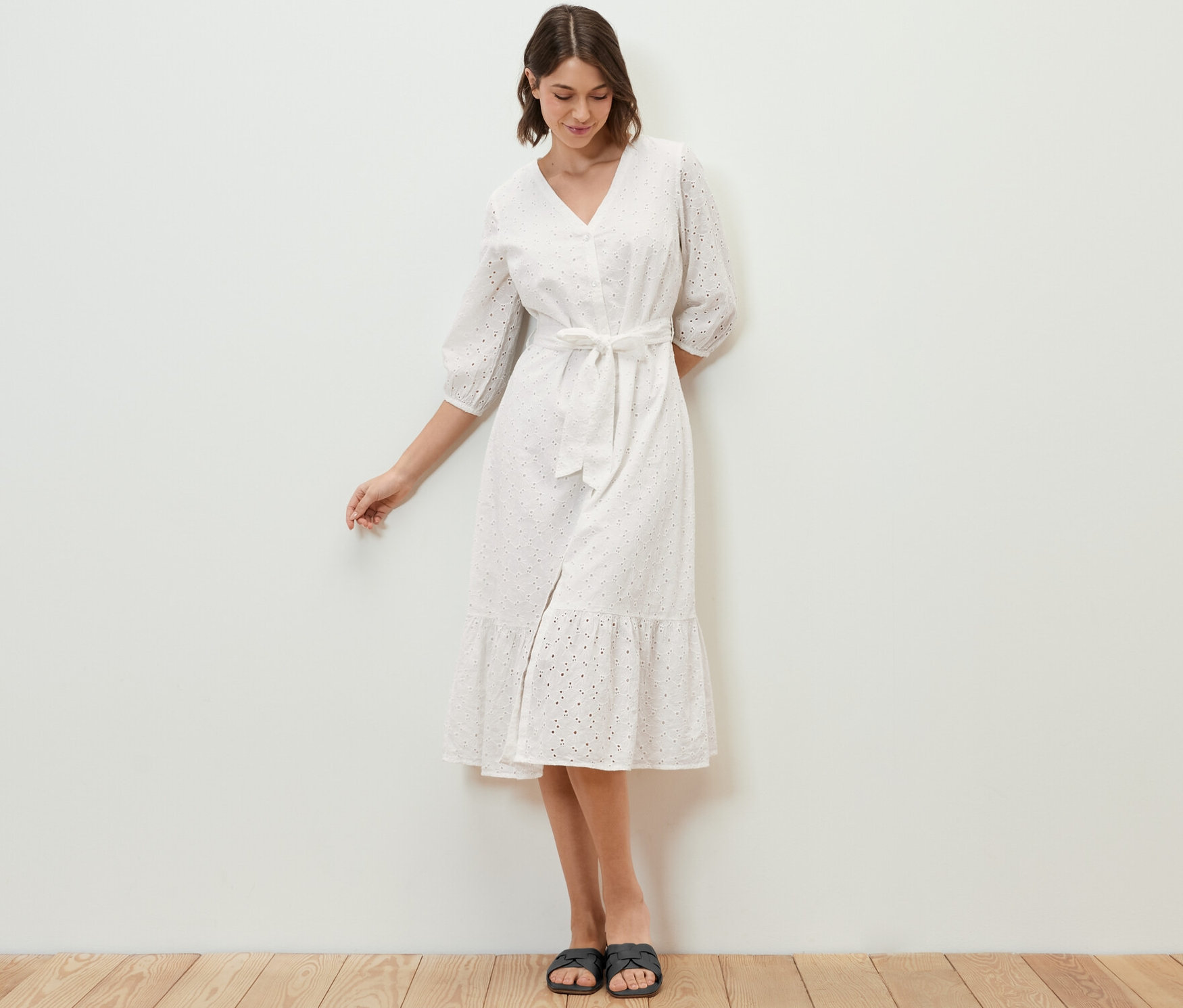 Kobieta stoi i ma na sobie sukienkę koszulową z haftem ażurowym.