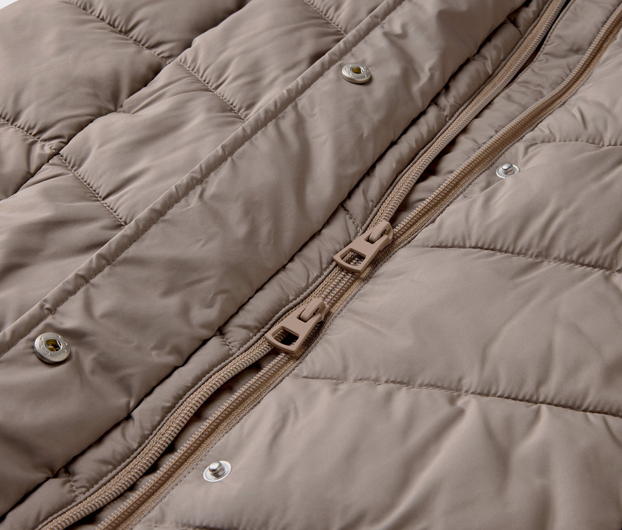Zbliżenie beżowej kurtki pikowanej z zamkiem błyskawicznym i zatrzaskami.