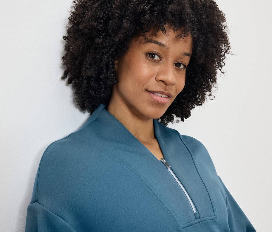 Portret uśmiechniętej kobiety z fryzurą afro w niebiesko-zielonej bluzie z zamkiem błyskawicznym.