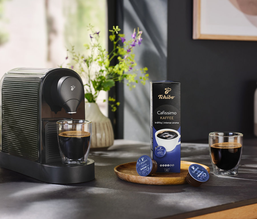 Czarny ekspres do kawy Cafissimo pure+ z filiżanką kawy i opakowaniem kapsułek do kawy.