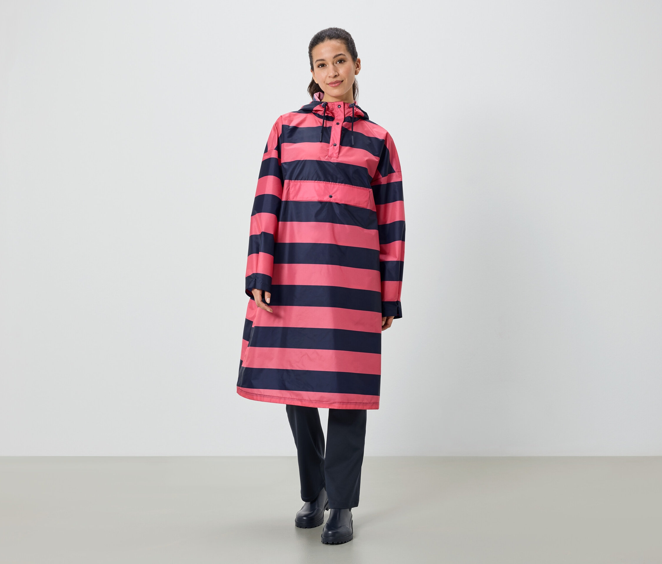 Kobieta stoi i ma na sobie płaszcz przeciwdeszczowy w paski różowo-granatowe.