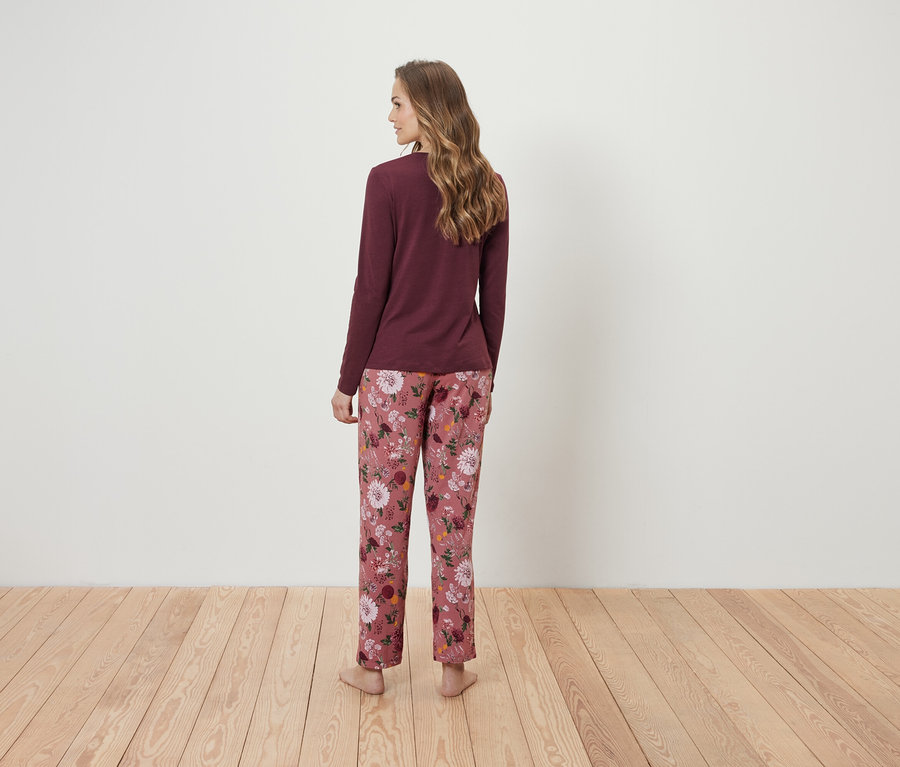 Kobieta tyłem do kamery ma na sobie bordową bluzkę z długim rękawem i różowe spodnie od piżamy w kwiaty.