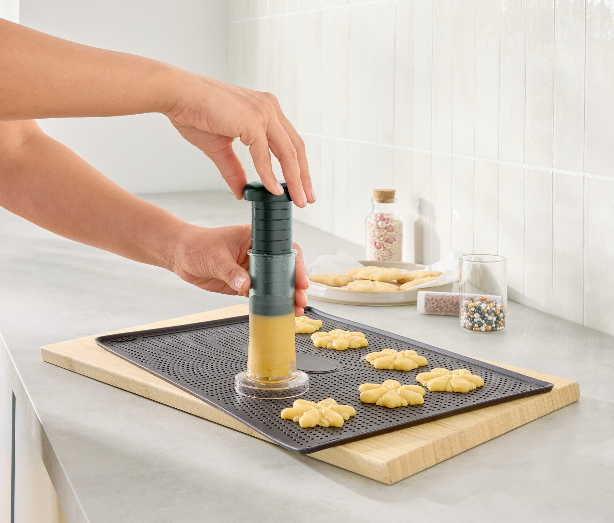 Kobieta używa praski do ciastek, aby uformować ciasto na blasze do pieczenia.