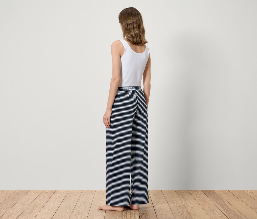 Kobieta stoi tyłem, ubrana w biały top i niebieskie spodnie w paski.