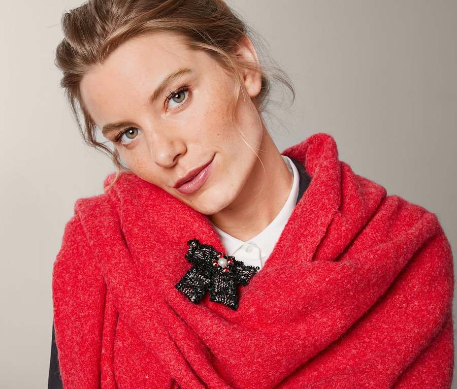 Kobieta w czerwonym szalu z broszką w kształcie kokardki z tweedu.