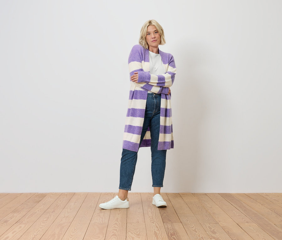 Blondwłosa kobieta stoi ze skrzyżowanymi ramionami. Ubrana jest w Mom Jeans – Fit »Nyla«, mid blue i pasiasty fioletowo-biały kardigan.