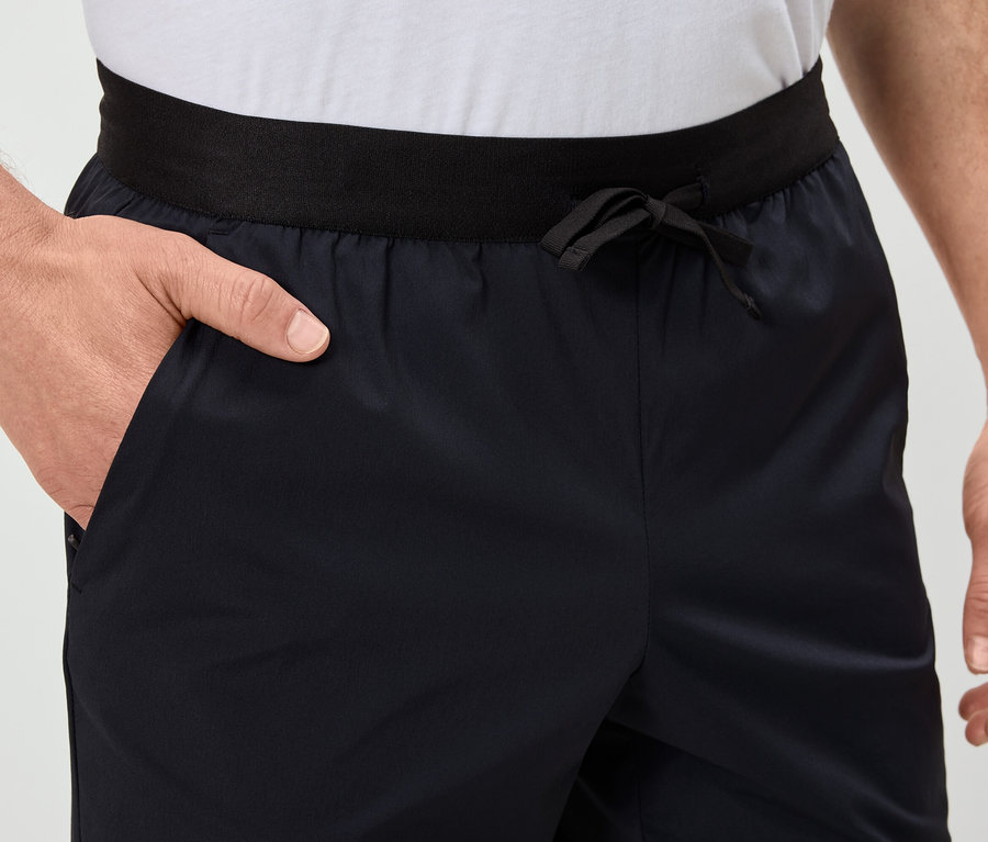 Mężczyzna trzyma rękę w kieszeni granatowych szortów z czarnym pasem.