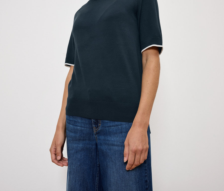 Kobieta ma na sobie granatowy top z krótkim rękawem i niebieskie dżinsy.