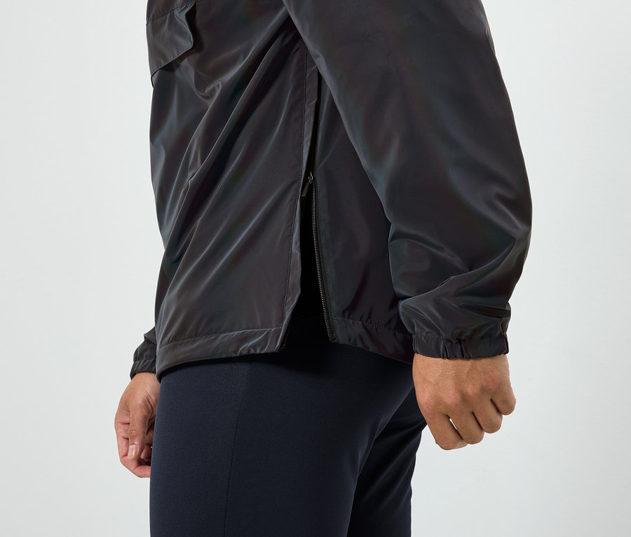 Mężczyzna ma na sobie błyszczącą kurtkę z rozpiętym zamkiem z boku i granatowe spodnie.