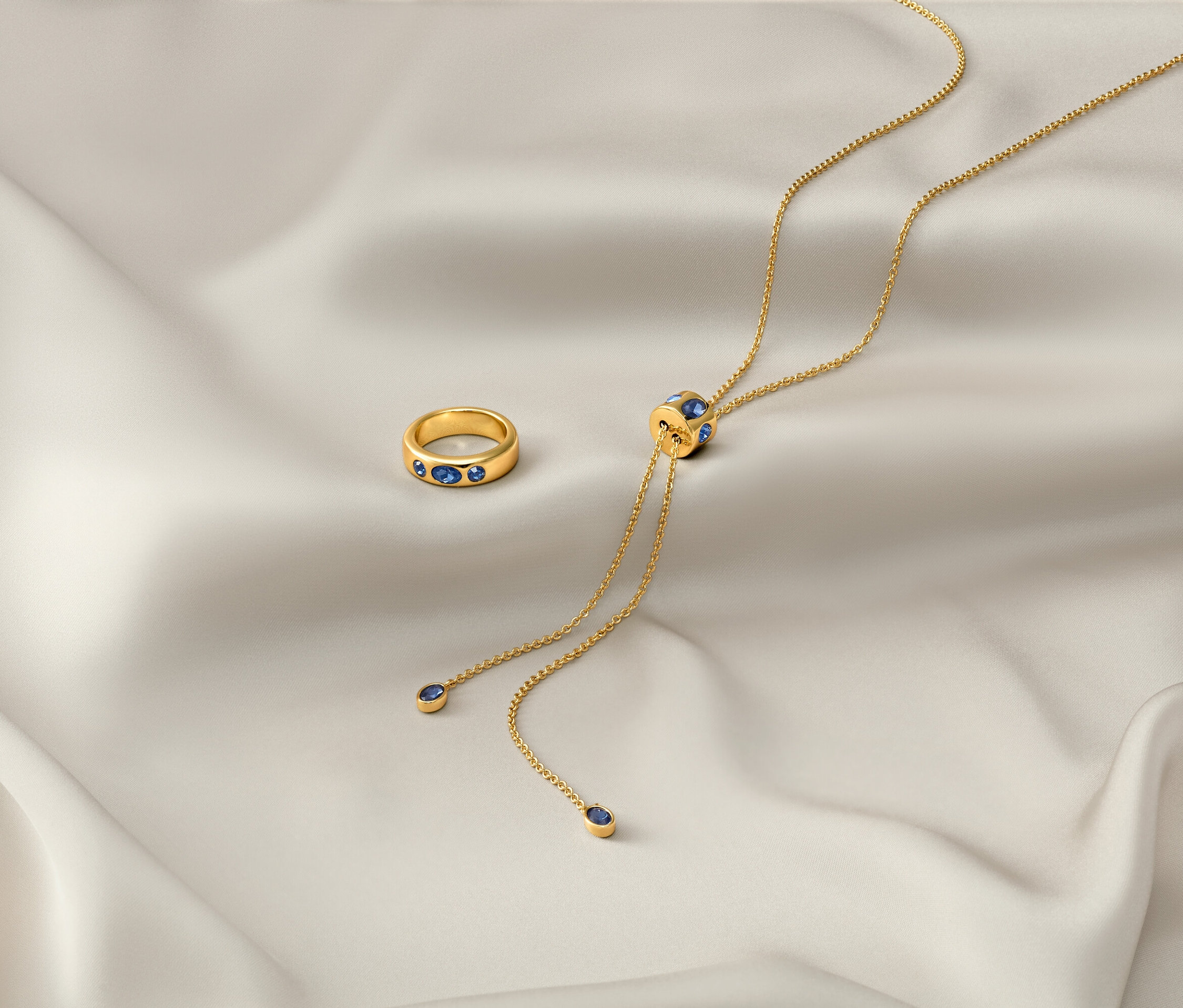 Na białej tkaninie leżą złoty łańcuszek »Iconic« i złoty pierścionek »Iconic«.