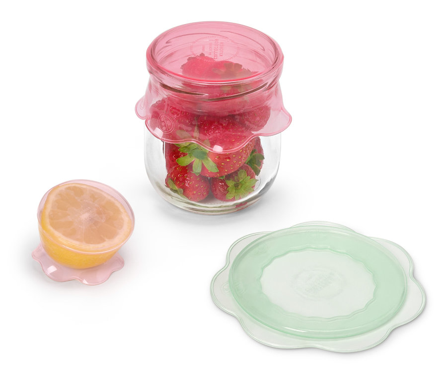 Słoik z truskawkami pod różową pokrywką stoi obok przekrojonej cytryny pod różową pokrywką i zielonej pokrywki.
