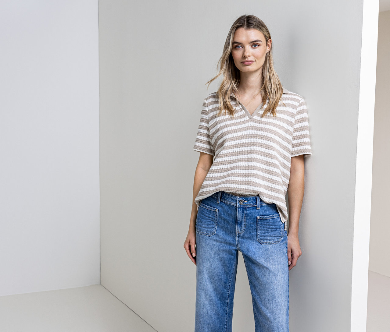 Kobieta pozuje w dżinsach i w paski, w koszulce z dzianiny Street One na tle ściany.