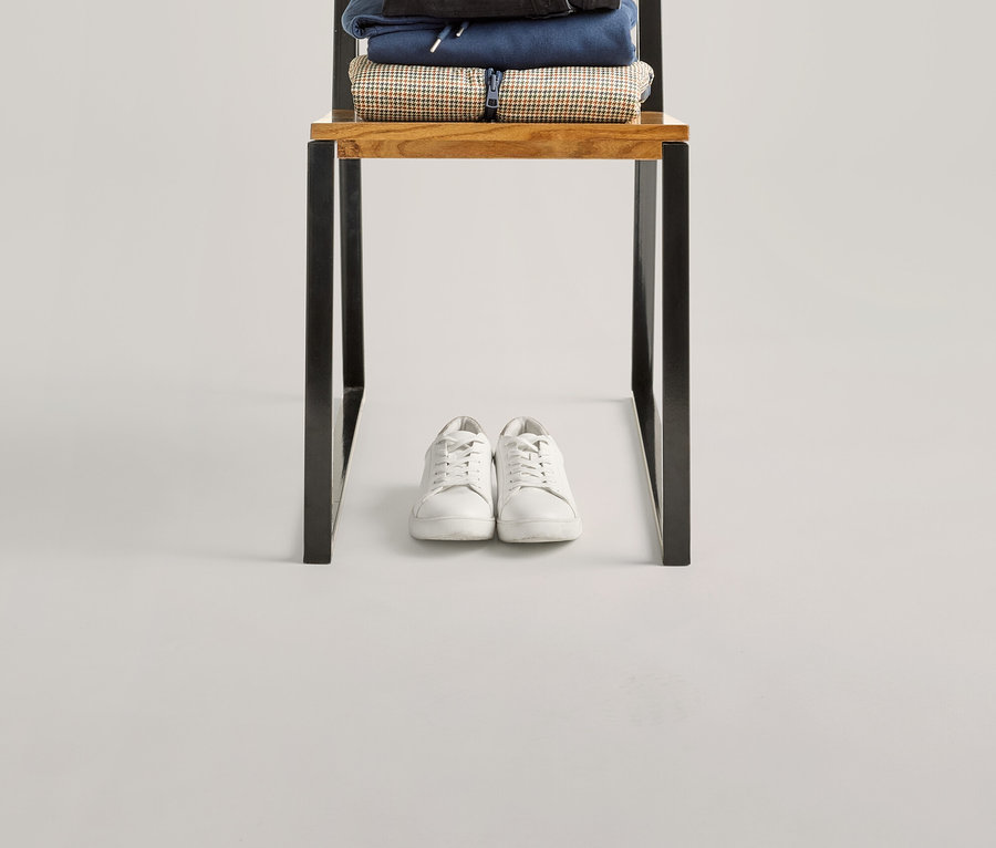 Na krześle leży granatowa torba na stosie ubrań, w tym koszulka z półdługim rękawem w zielone paski i białe tenisówki.