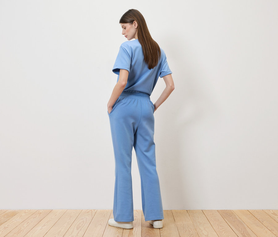 Kobieta stoi tyłem do kamery, ma na sobie jasno-niebieski T-shirt i pasujące spodnie