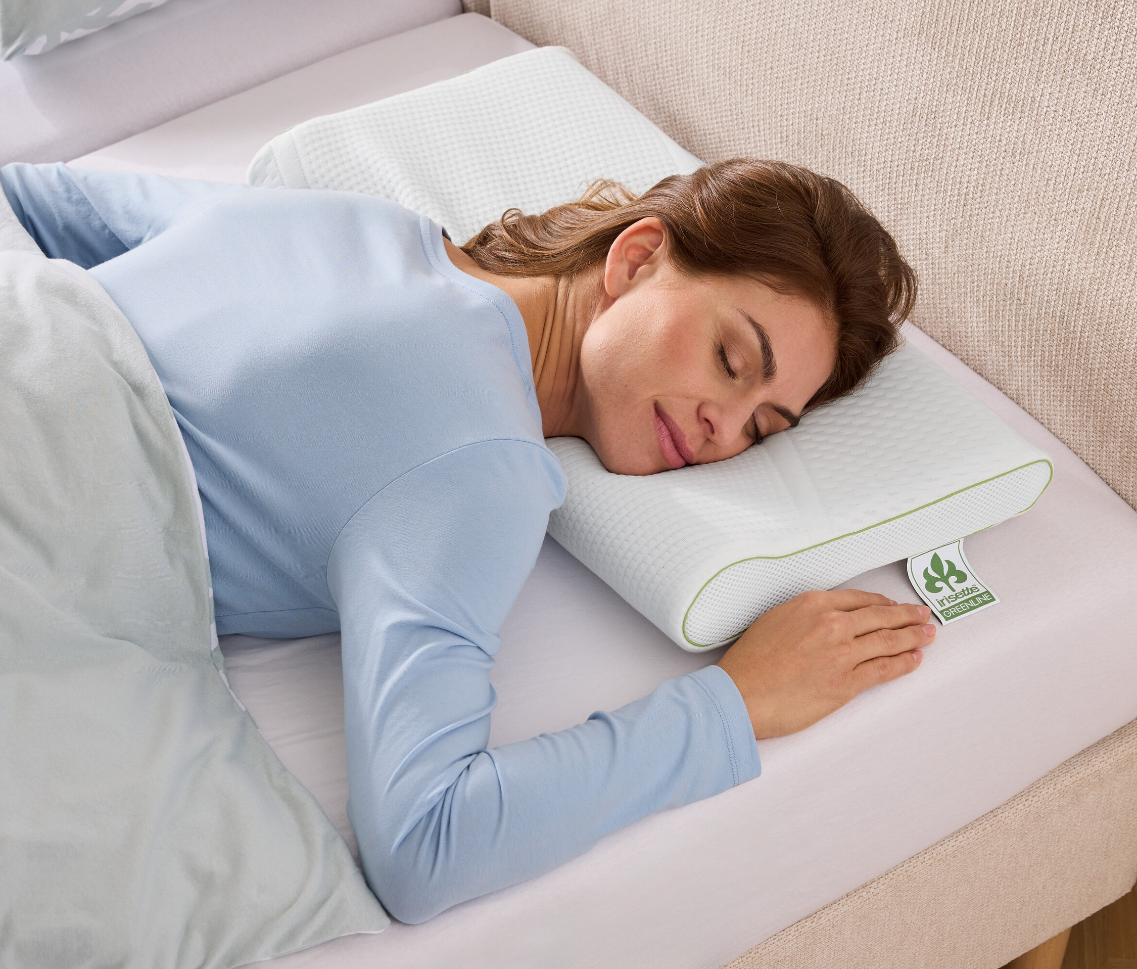 Kobieta śpi na teksturowanej, białej poduszce z zielonymi akcentami w łóżku z jasnoniebieską pościelą.