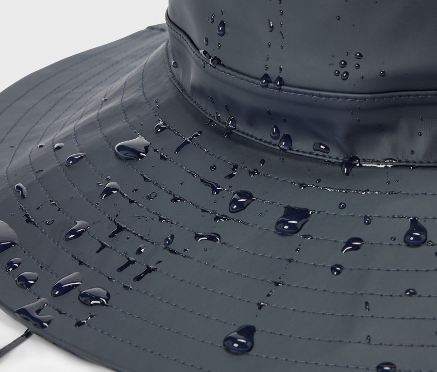 Zbliżenie na granatowy kapelusz typu bucket hat z widocznymi kroplami wody.