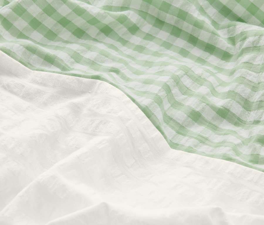 Zbliżenie pogniecionej pościeli: jedna część jest biała, druga zielono-biała w kratę.