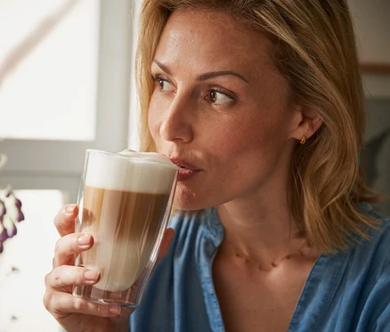 Kobieta pije latte macchiato ze szklanki o podwójnych ściankach.
