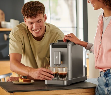 Mężczyzna patrzy, jak kawa wlewa się do dwóch szklanek z automatycznego ekspresu do kawy »Esperto2 Caffè« w kolorze titanium silver.