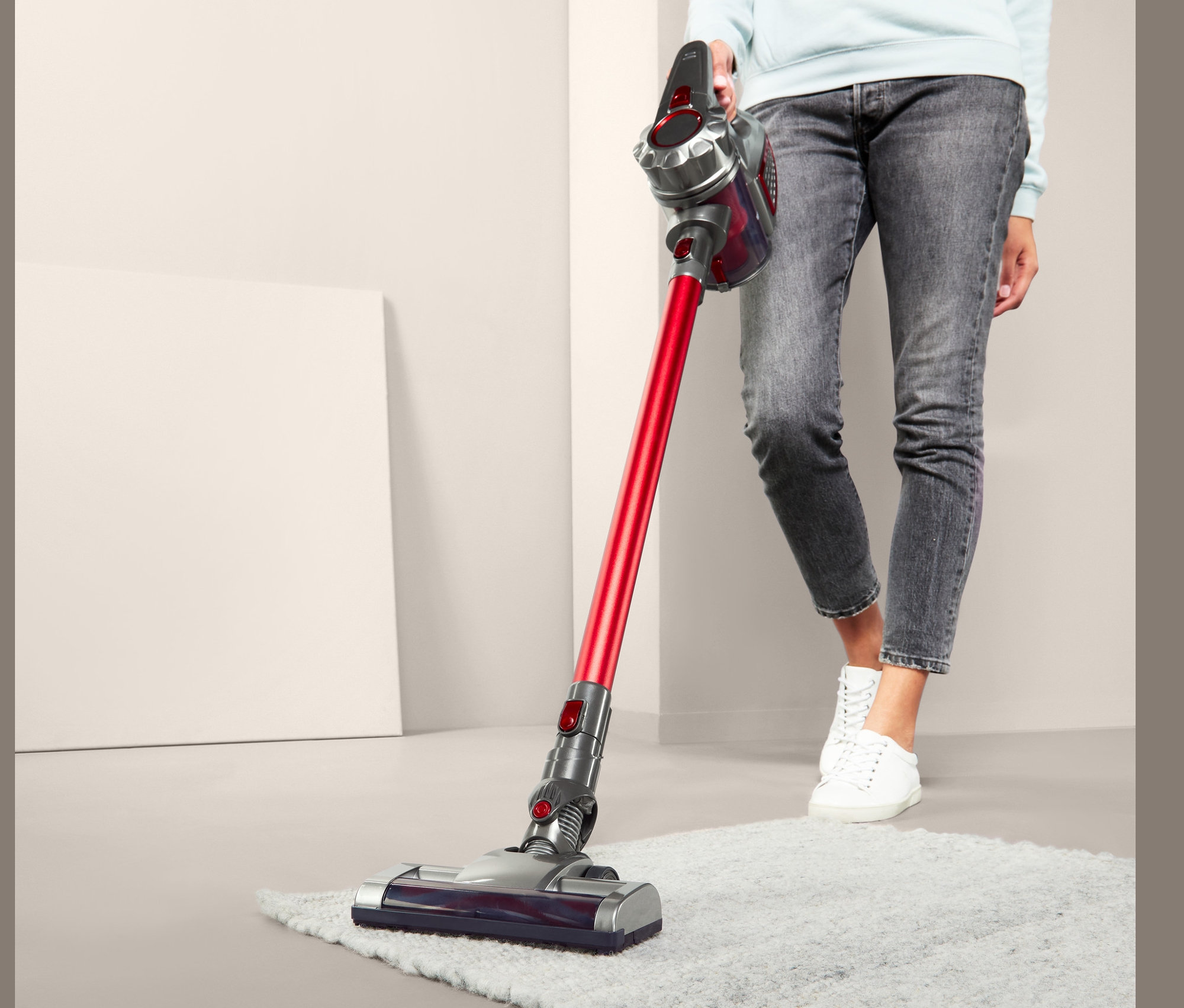 Kobieta odkurza puszysty dywan bezprzewodowym odkurzaczem akumulatorowym, z 4 wymiennymi końcówkami.