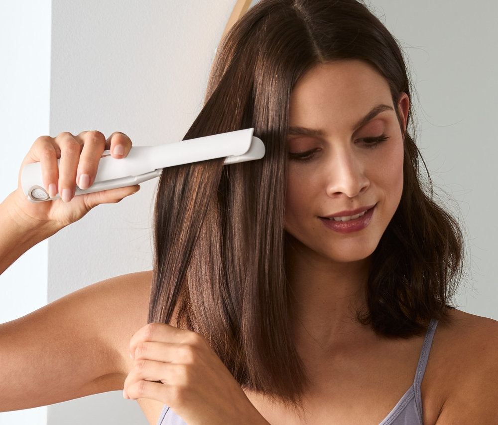 Kobieta prostuje włosy bezprzewodową prostownicą.