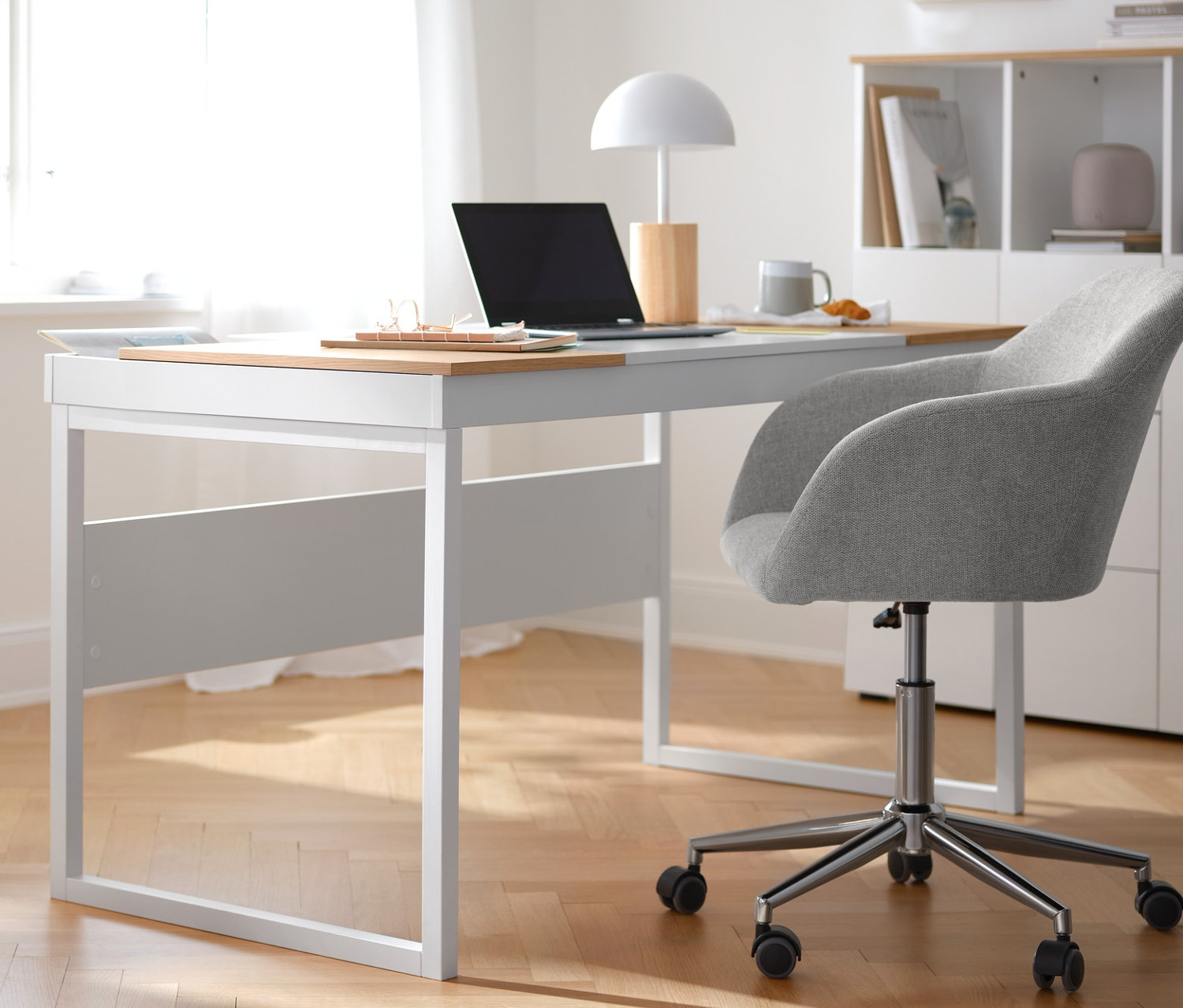 Beżowe krzesło do biurka stoi przy białym biurku. Po lewej stronie znajduje się kontener na kółkach z półką. W tle półotwarta szafka typu highboard.