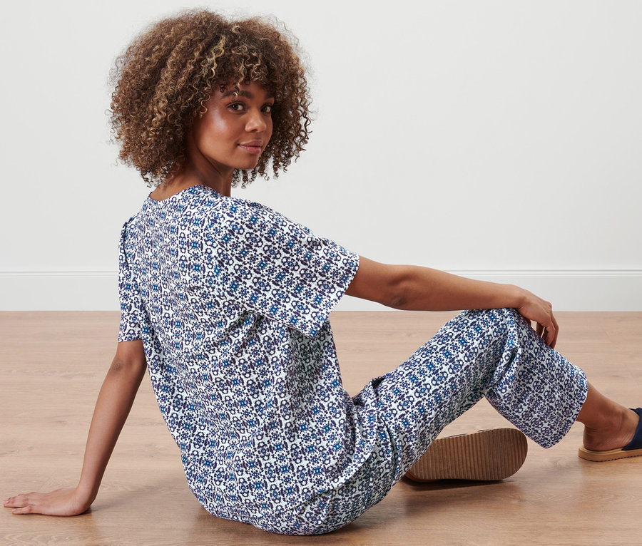 Kobieta siedzi na podłodze w bluzce z nadrukiem na całej powierzchni i spodniach.