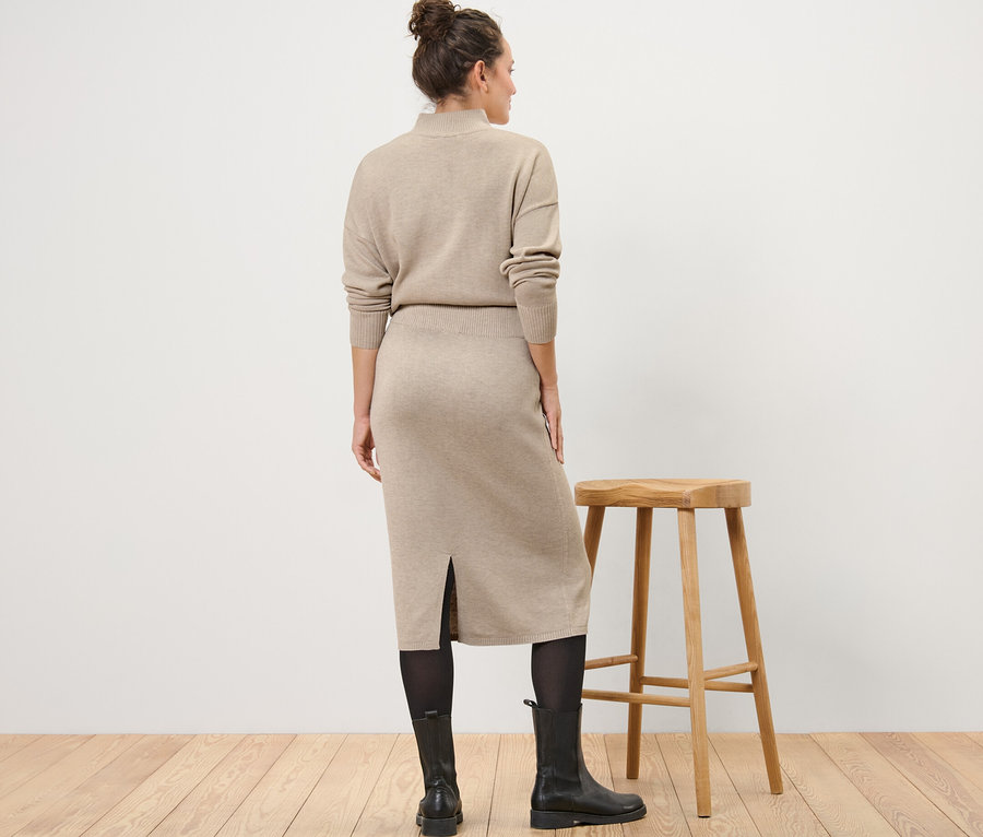 Kobieta stoi tyłem, ma na sobie spódnicę z dzianiny, rajstopy i buty.