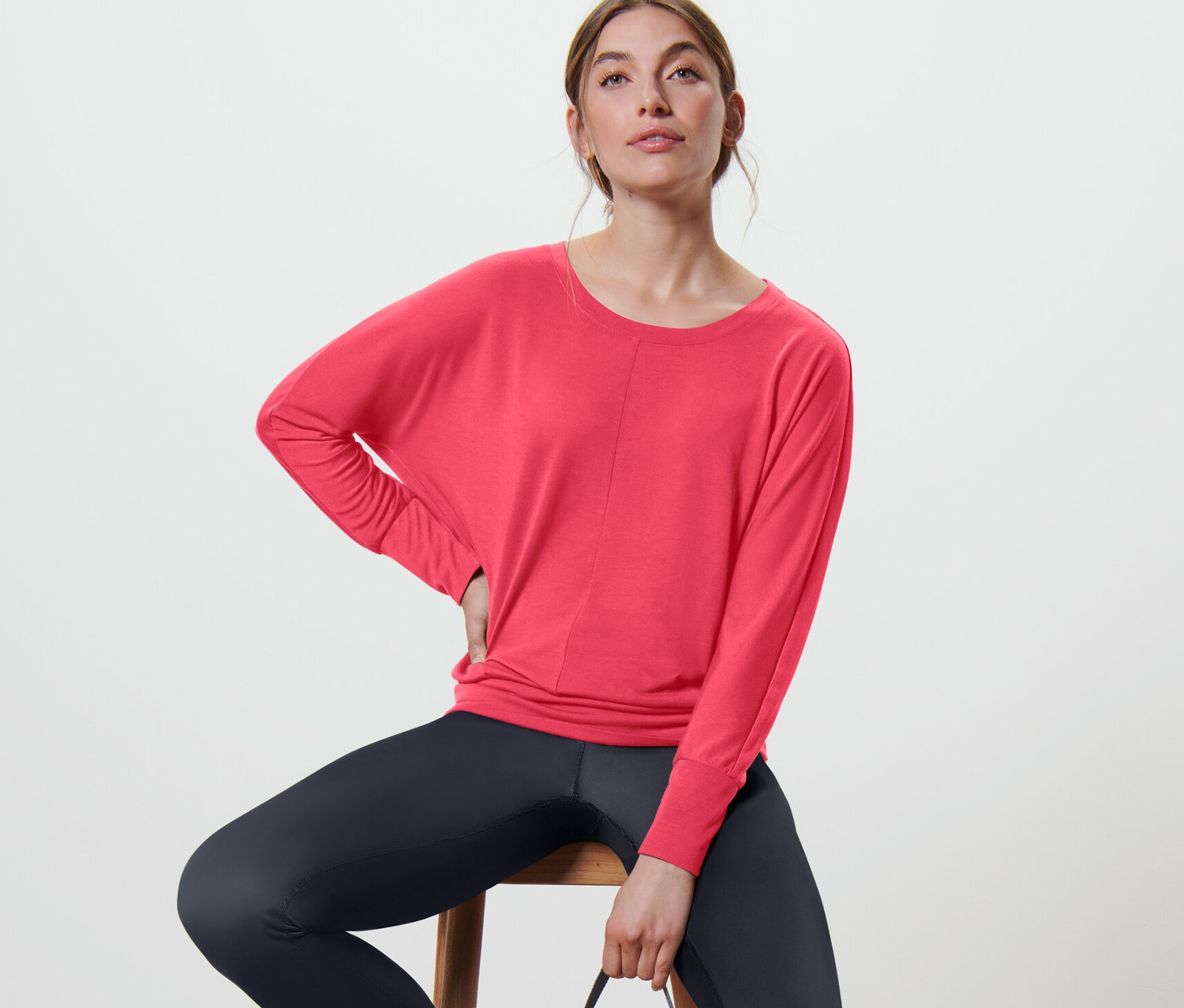 Kobieta siedzi na krześle i ma na sobie różową koszulkę do sportu i jogi.