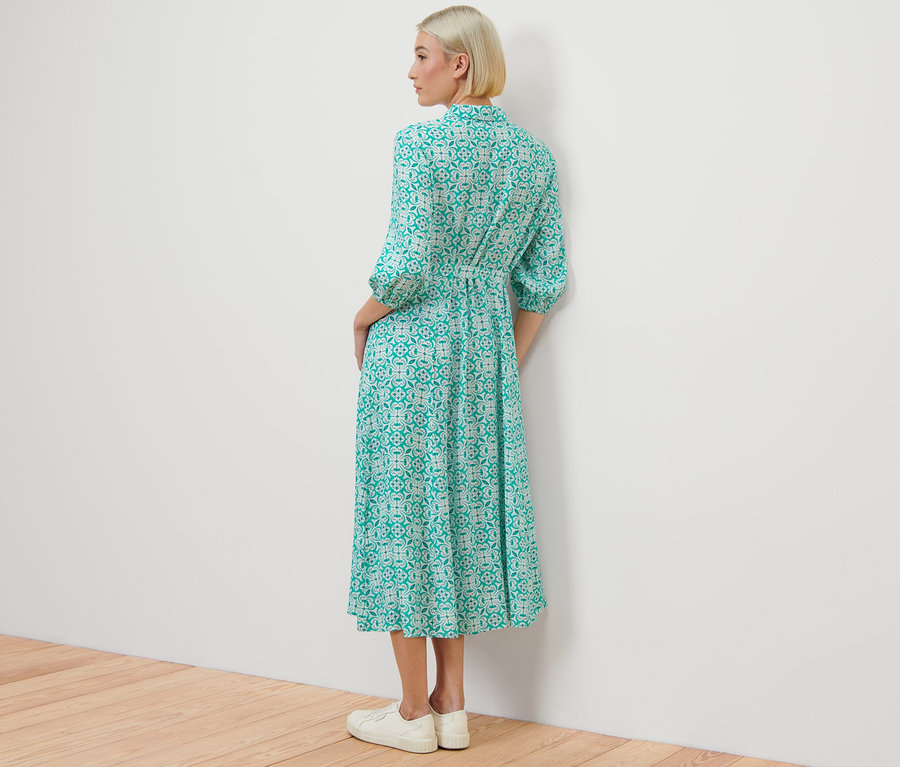 Kobieta stoi tyłem, ubrana w sukienkę koszulową ze wzorem na całej powierzchni.