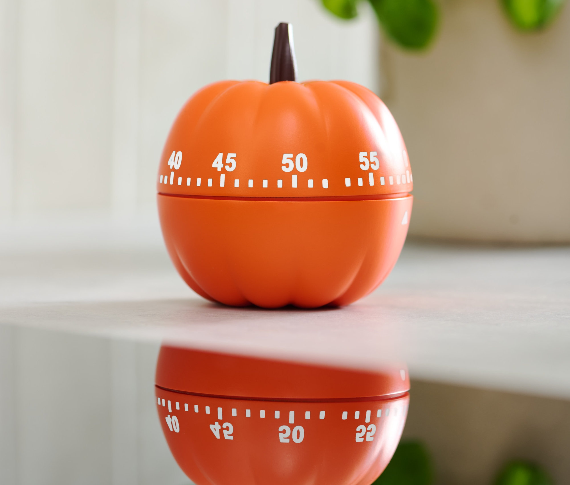 Pomarańczowy minutnik w kształcie dyni na błyszczącej powierzchni.