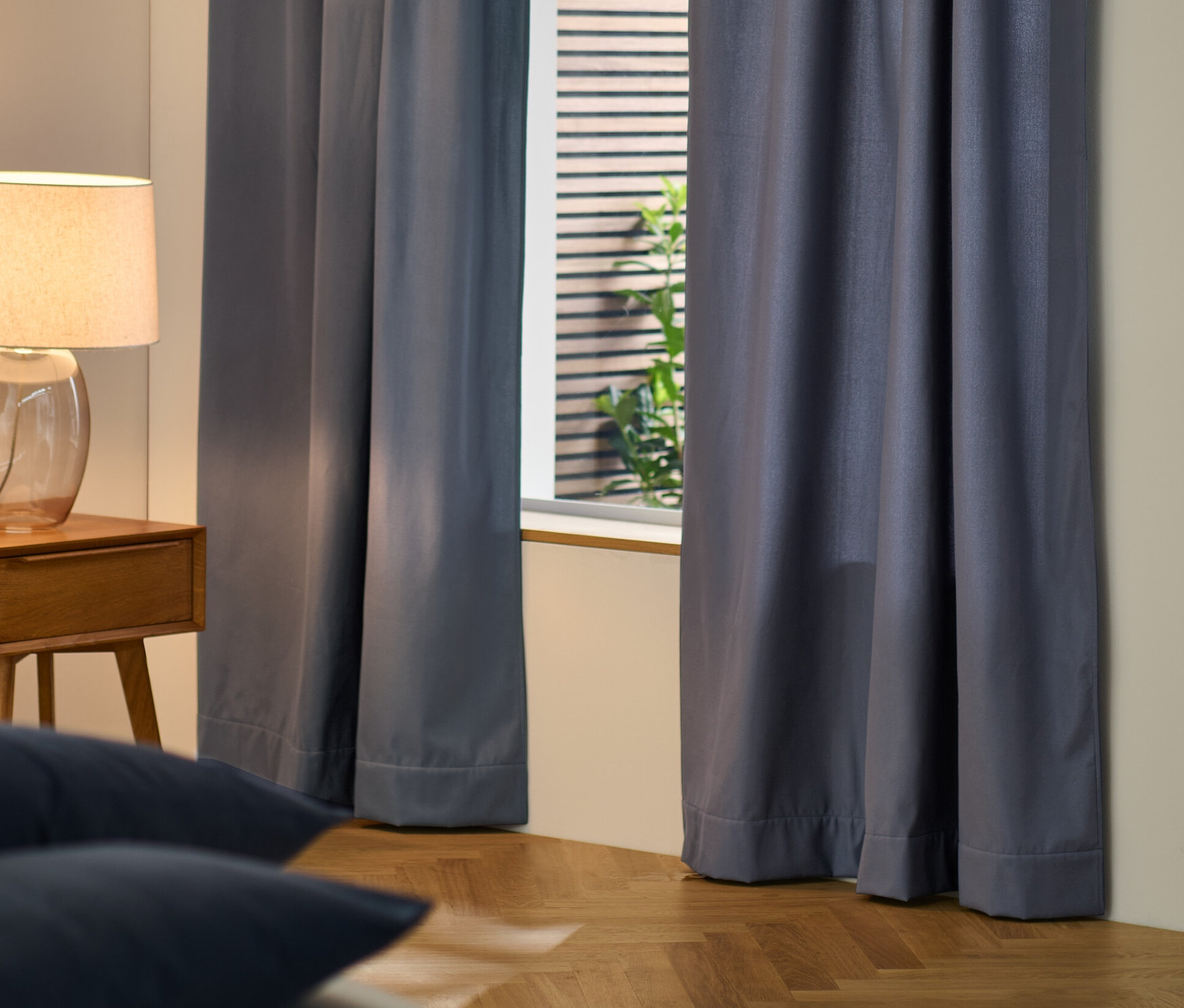 Niebieskie zasłony termiczne zakrywają okno w sypialni.